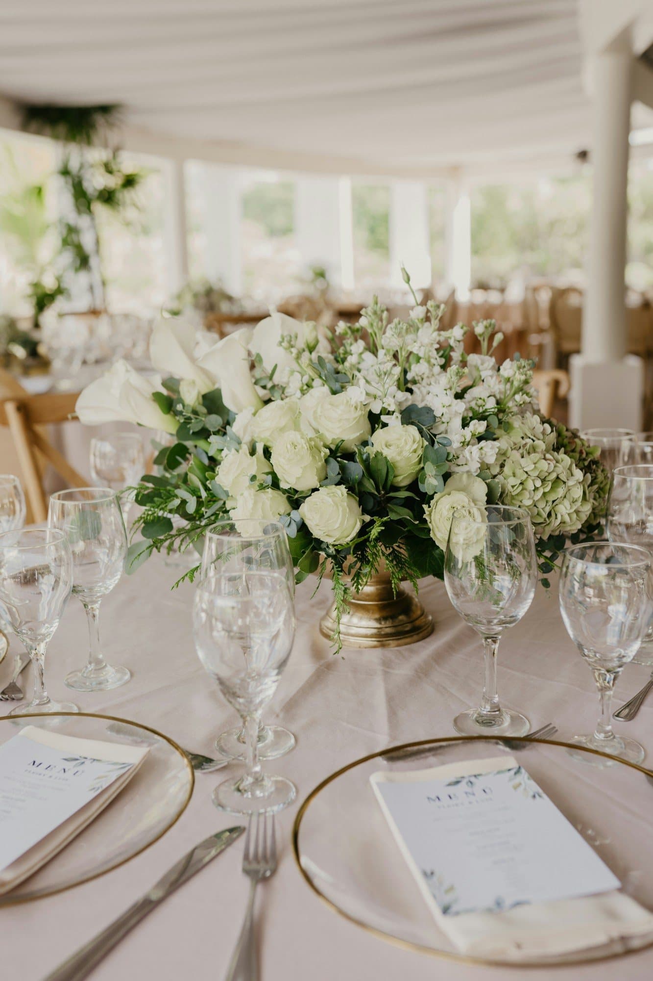 Une table de mariage dressée, un centre de table de roses blanches et d'eucalyptus, les menus posés sur les assiettes